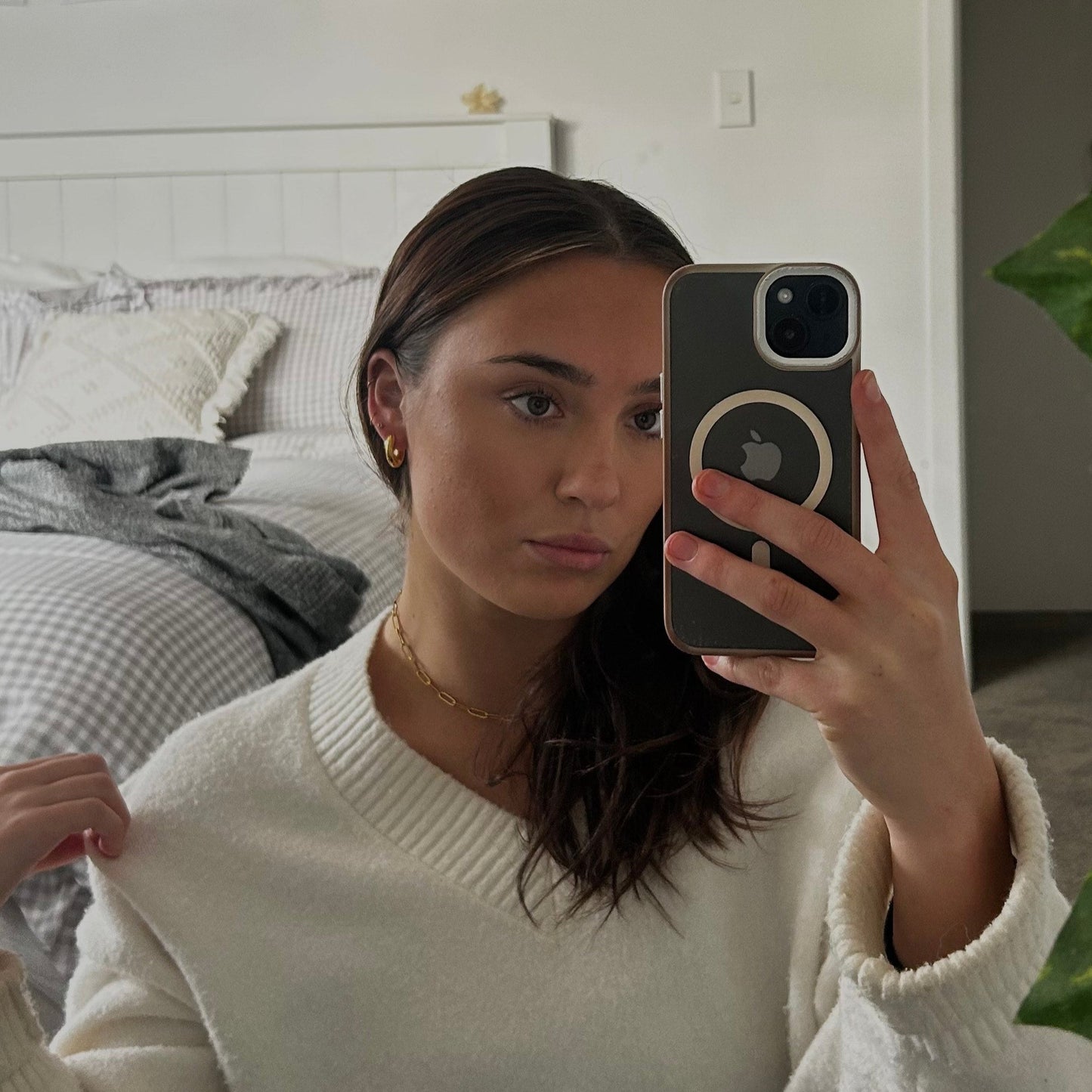 Woman taking a mirror selfie in a bedroom holding a phone with a white case.