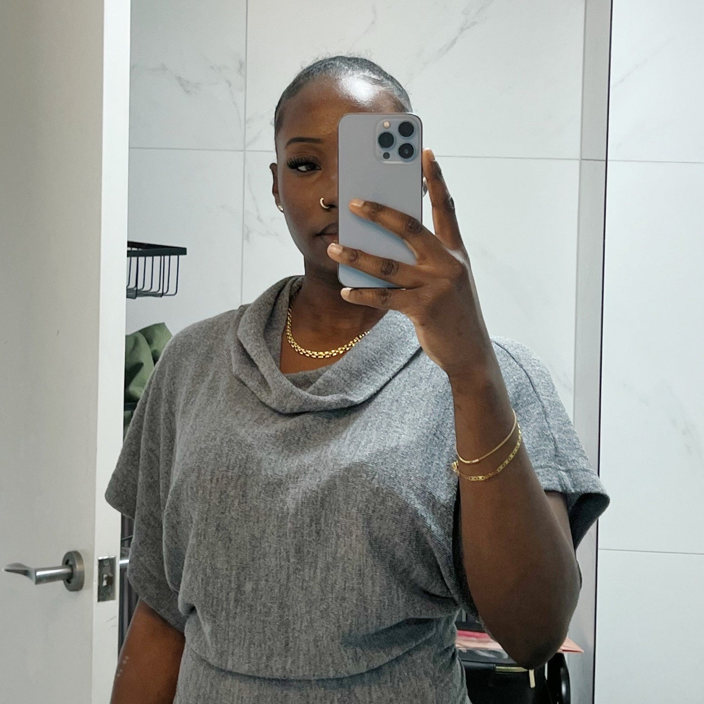 Person taking a mirror selfie wearing a gray outfit with a gold necklace and bracelet.