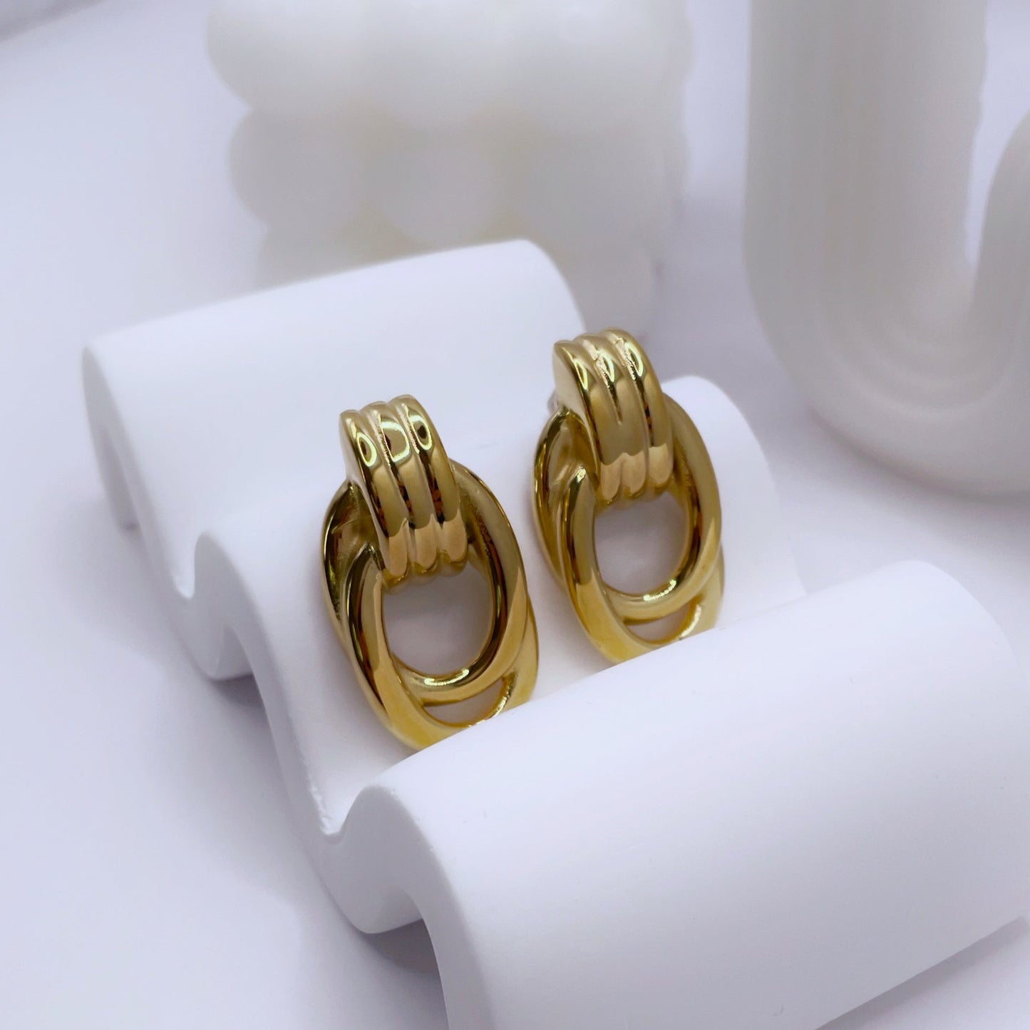 Gold hoop earrings on a white stand with white candles in the background